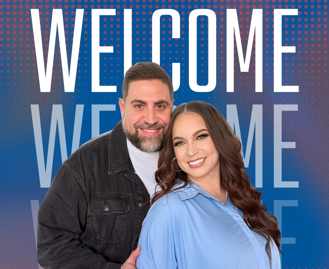 Smiling man and woman stand together in front of a blue gradient backdrop with large 'WELCOME' text behind them (welcome banner).