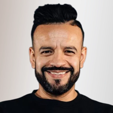 Smiling man with dark hair and a beard, wearing a black shirt, against a light background (head-and-shoulders portrait).