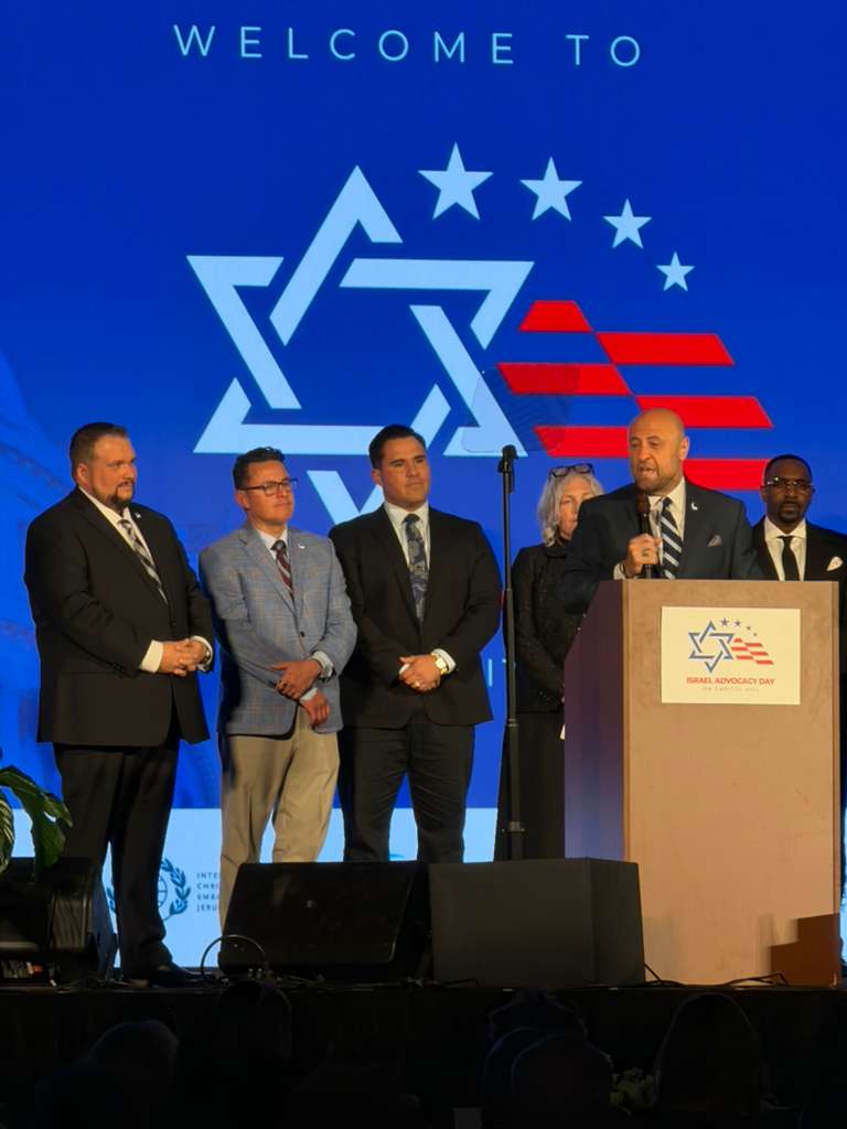 Group of five speakers on stage at Israel Advocacy Day, with a blue backdrop featuring a Star of David logo and a podium.