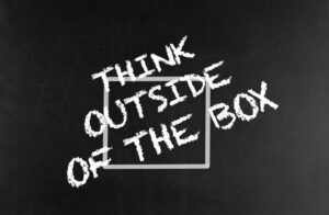 Chalkboard with the phrase "Think outside the box" written around a gray square outline, conveying a creative thinking message.