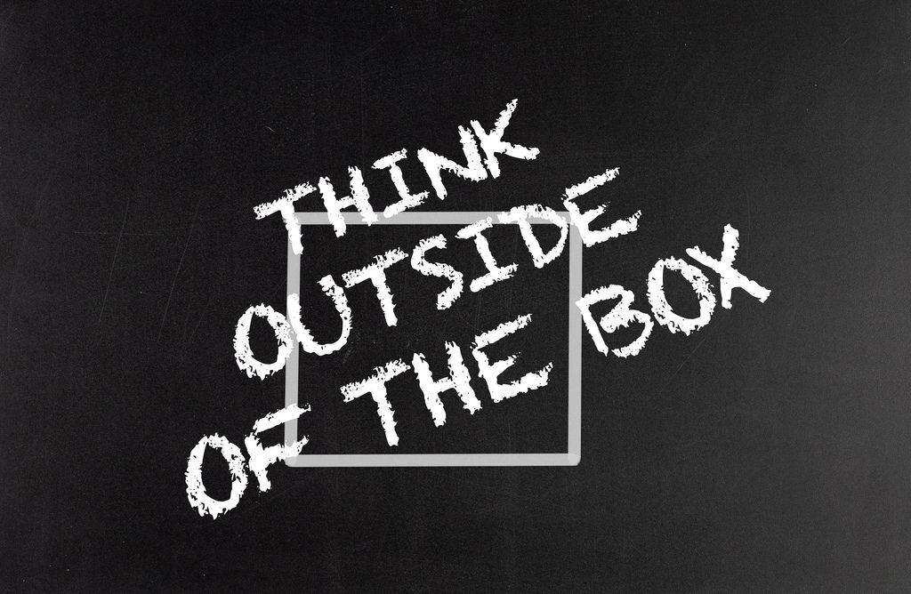 Chalkboard with the phrase "Think outside the box" written around a gray square outline, conveying a creative thinking message.