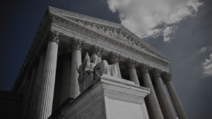 White marble courthouse facade with tall Corinthian columns and a seated statue on a pedestal beneath a pediment, viewed from below.