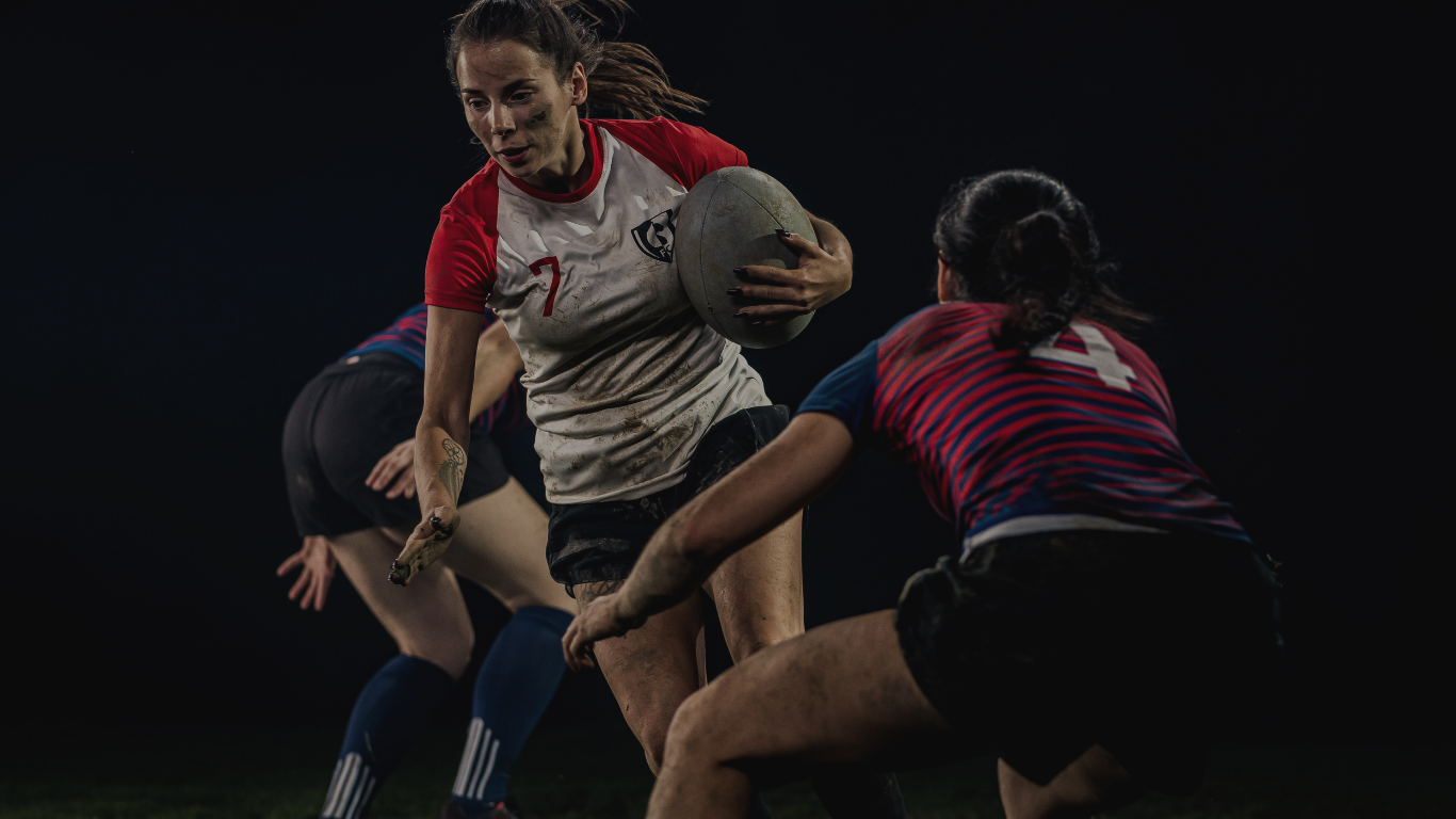 Rugby player in white-red jersey with the ball runs forward as a striped-team defender closes in under stadium lights at night.