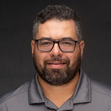 Portrait of a smiling man with glasses and a trimmed beard, wearing a gray polo shirt.