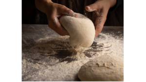 Hands shaping a round dough on a flour-dusted counter edge to edge of the image.
