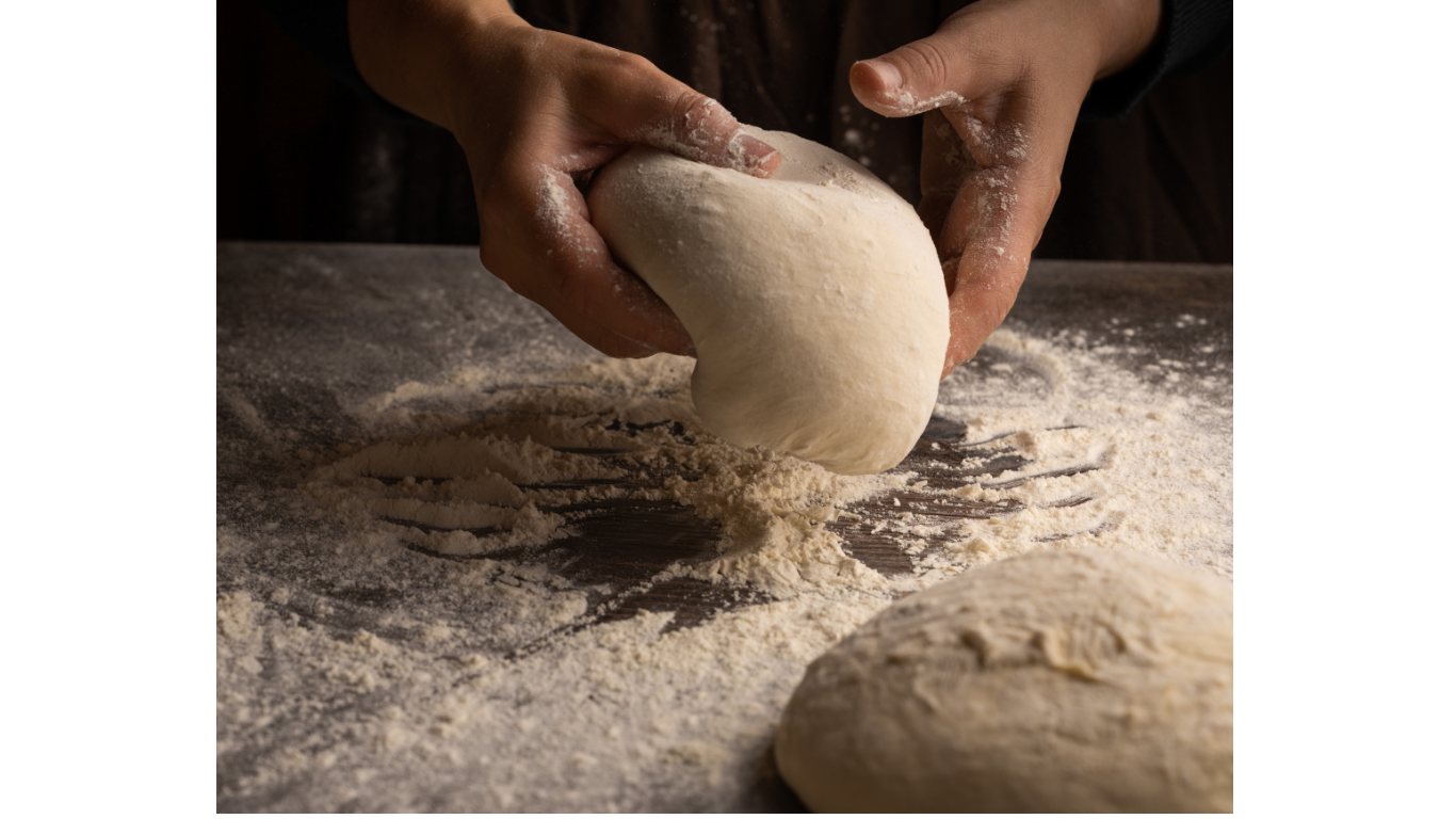 Hands shaping a round dough on a flour-dusted counter edge to edge of the image.