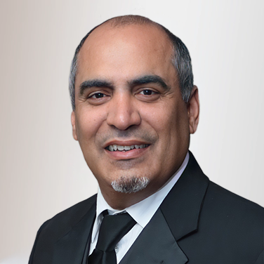 Head-and-shoulders portrait of a smiling middle-aged man in a black suit and tie against a light gradient background.