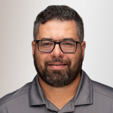 Man with short dark hair and a beard wearing black glasses and a gray polo shirt, smiling at the camera.