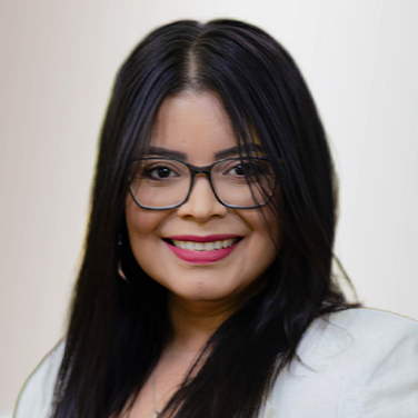 Portrait of a smiling woman with long dark hair and black-rimmed glasses, wearing a light blazer. (Headshot)