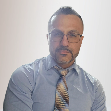 Professional portrait of a man with short dark hair and glasses, wearing a light blue dress shirt and striped tie, looking at the camera.