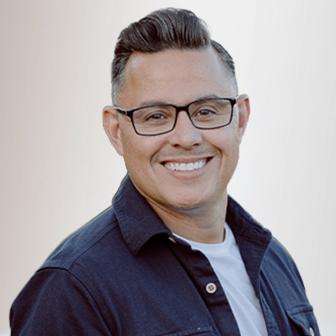 Smiling man with glasses wearing a navy shirt, head-and-shoulders portrait against a light background, front-facing pose.