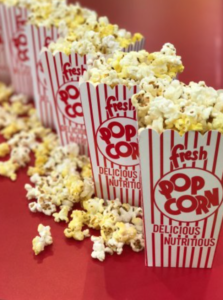 Row of striped red-and-white popcorn boxes labeled 'Popcorn' with popcorn spilling onto a red table, a snack display scene.